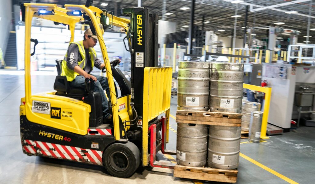 pexels-photo-1267337-1267337 Forklift operator in warehouse moving beer kegs for distribution.